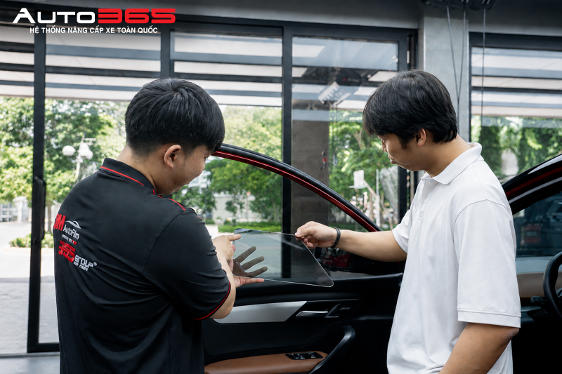 Kỹ thuật viên cùng khách hàng kiểm tra phim tại vị trí kính cửa, minh họa bước đối chiếu độ sáng và khả năng quan sát trước khi nhận xe